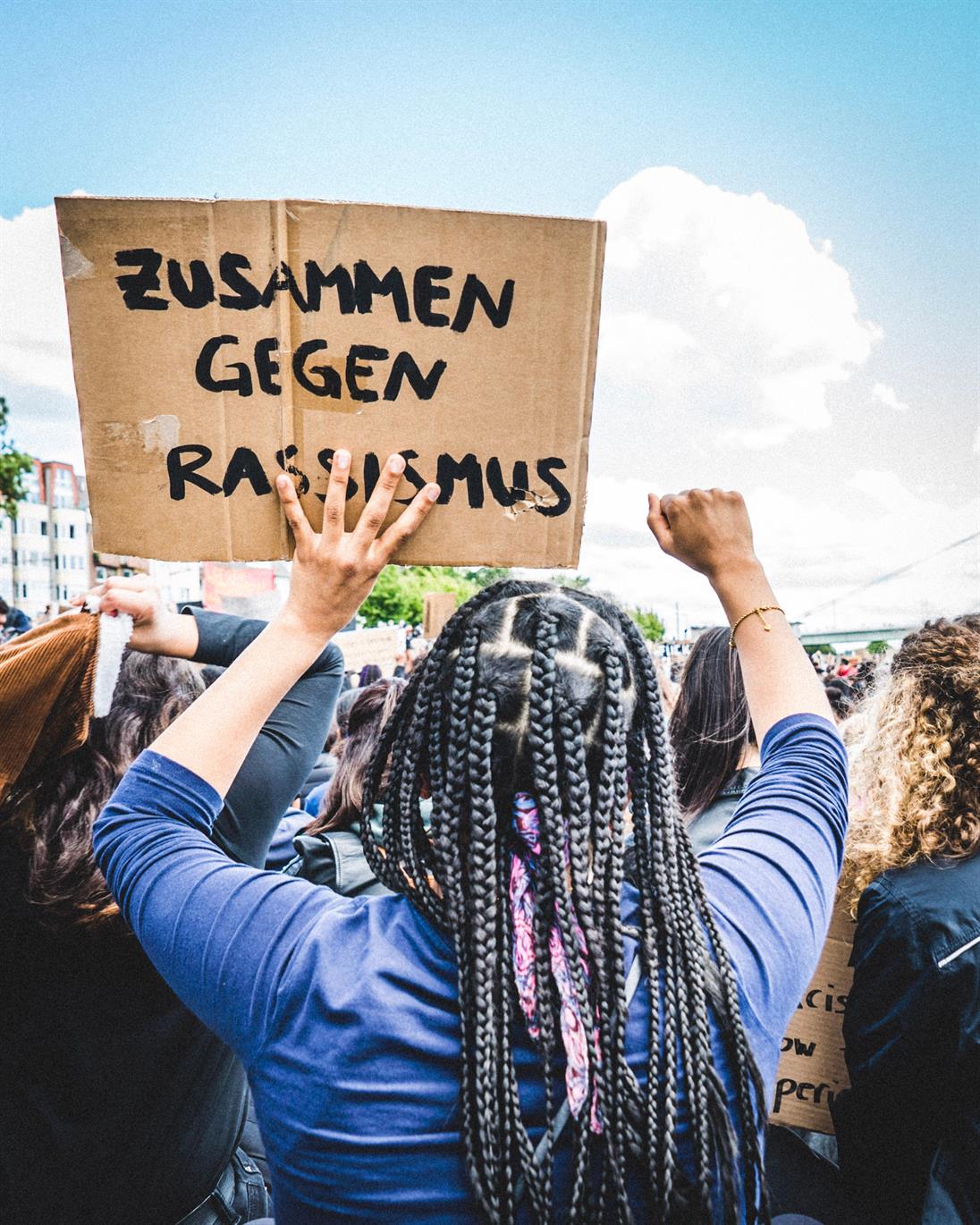 Ein Bild von einer Frau, welche man von hinten sieht und die ein Schild hochhält mit der Aufschrift "Zusammen gegen Rassismus"